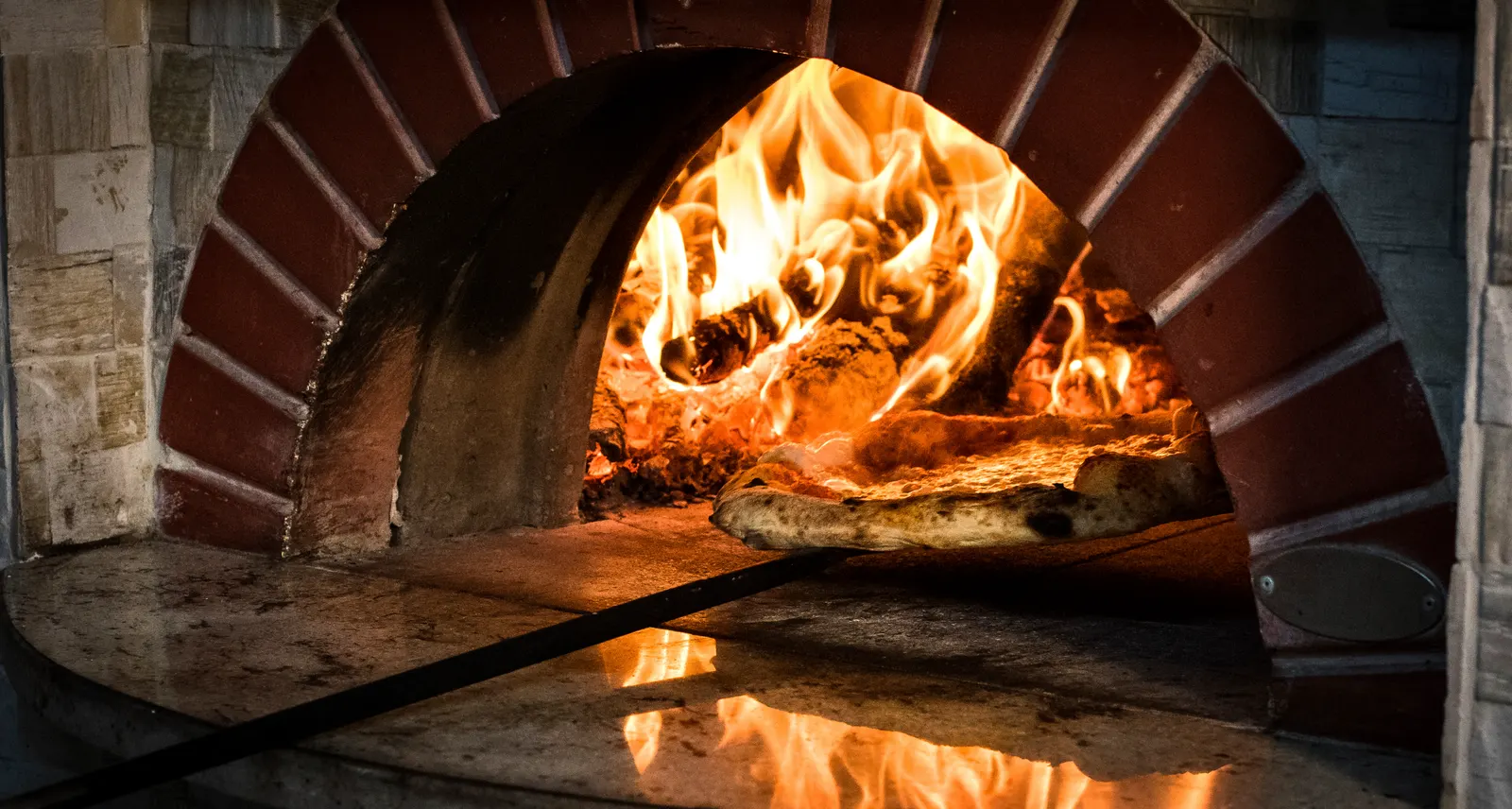Pizza baking in a stone oven with open flames