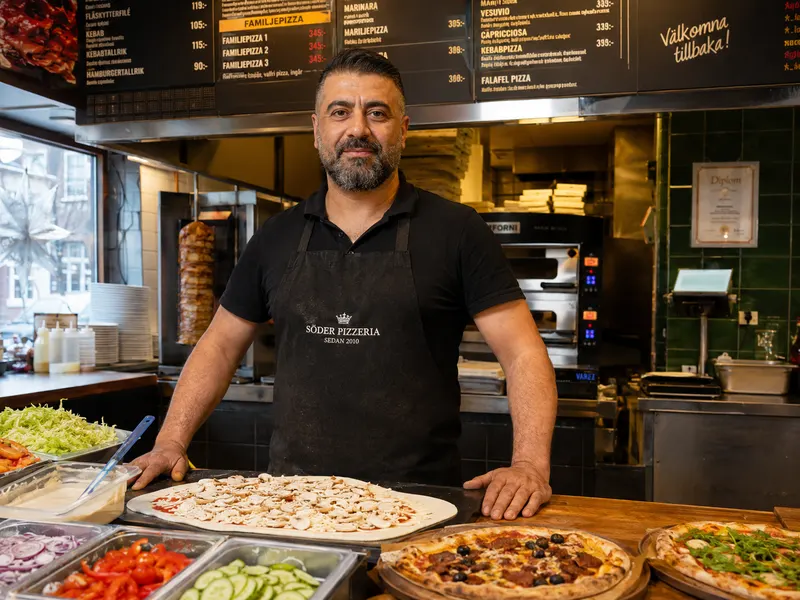 Pizzeriaägare bakom disken med meny i bakgrunden
